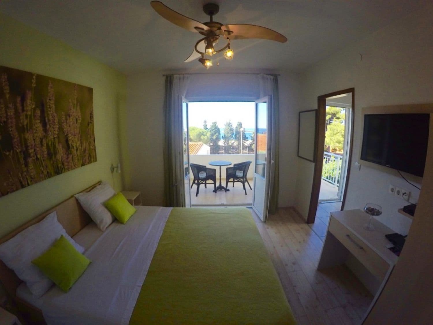 Habitación de hotel con cama, ventilador de techo, televisión y balcón con mesa y sillas.