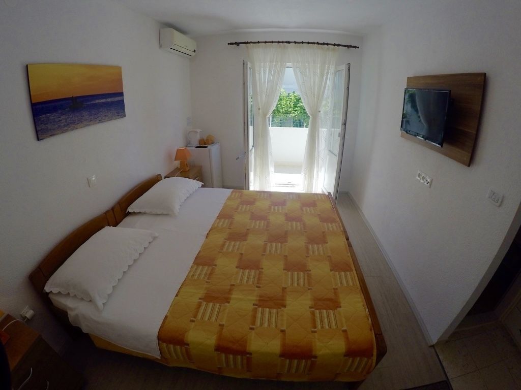 Een slaapkamer met een bed, een aan de muur bevestigde televisie en een raam met gordijnen.
