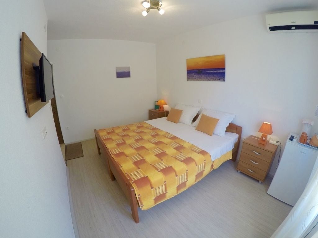 Een slaapkamer met een bed, nachtkastjes, een televisie, een schilderij en een koelkast.