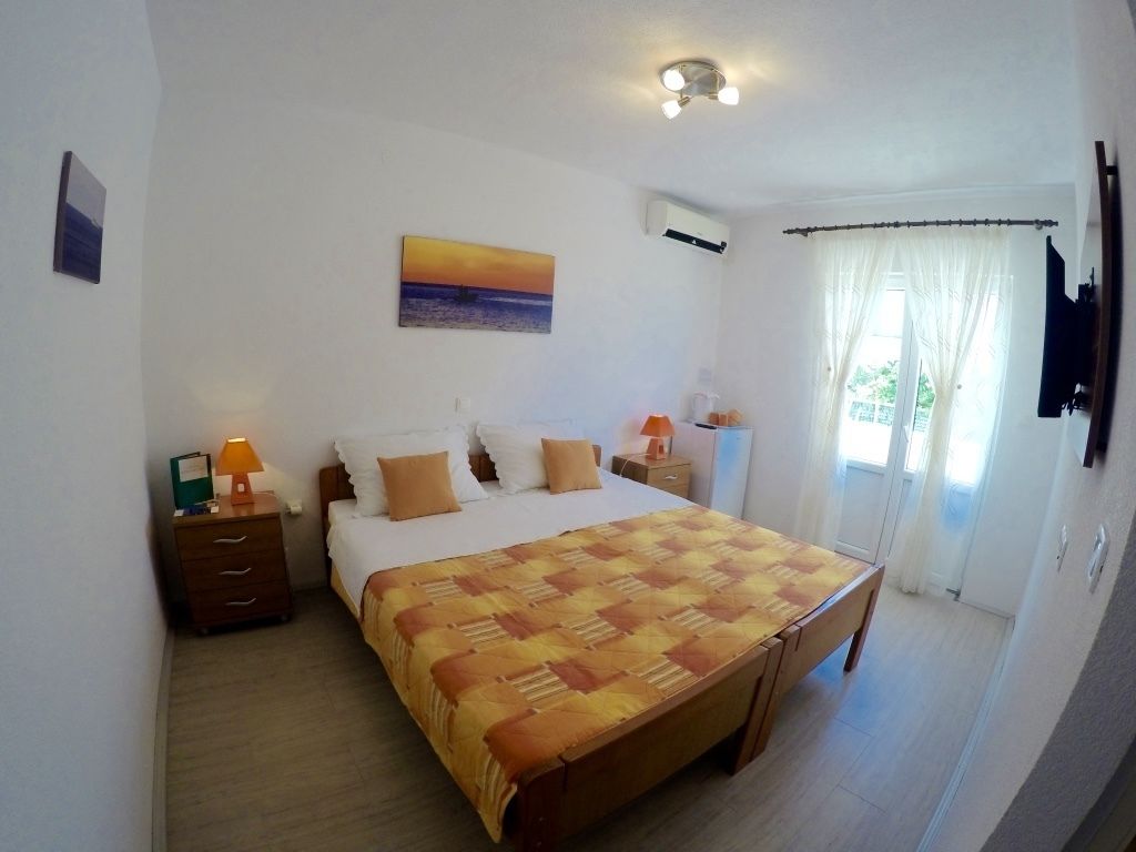 A bedroom with a large bed, a nightstand, a lamp, a painting on the wall, and a window with curtains.