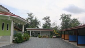 A building with a covered outdoor area, gravel ground, and surrounding greenery.