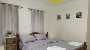 A neatly made bed with a wooden headboard, a small bedside table with a vase of flowers, and a shelf below.