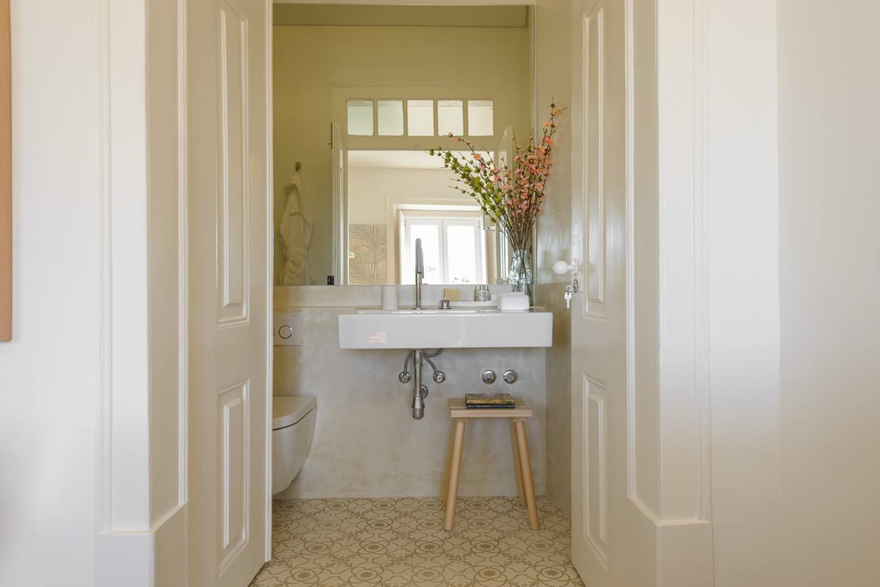 Une salle de bain avec un lavabo blanc, un miroir au-dessus et un petit tabouret.