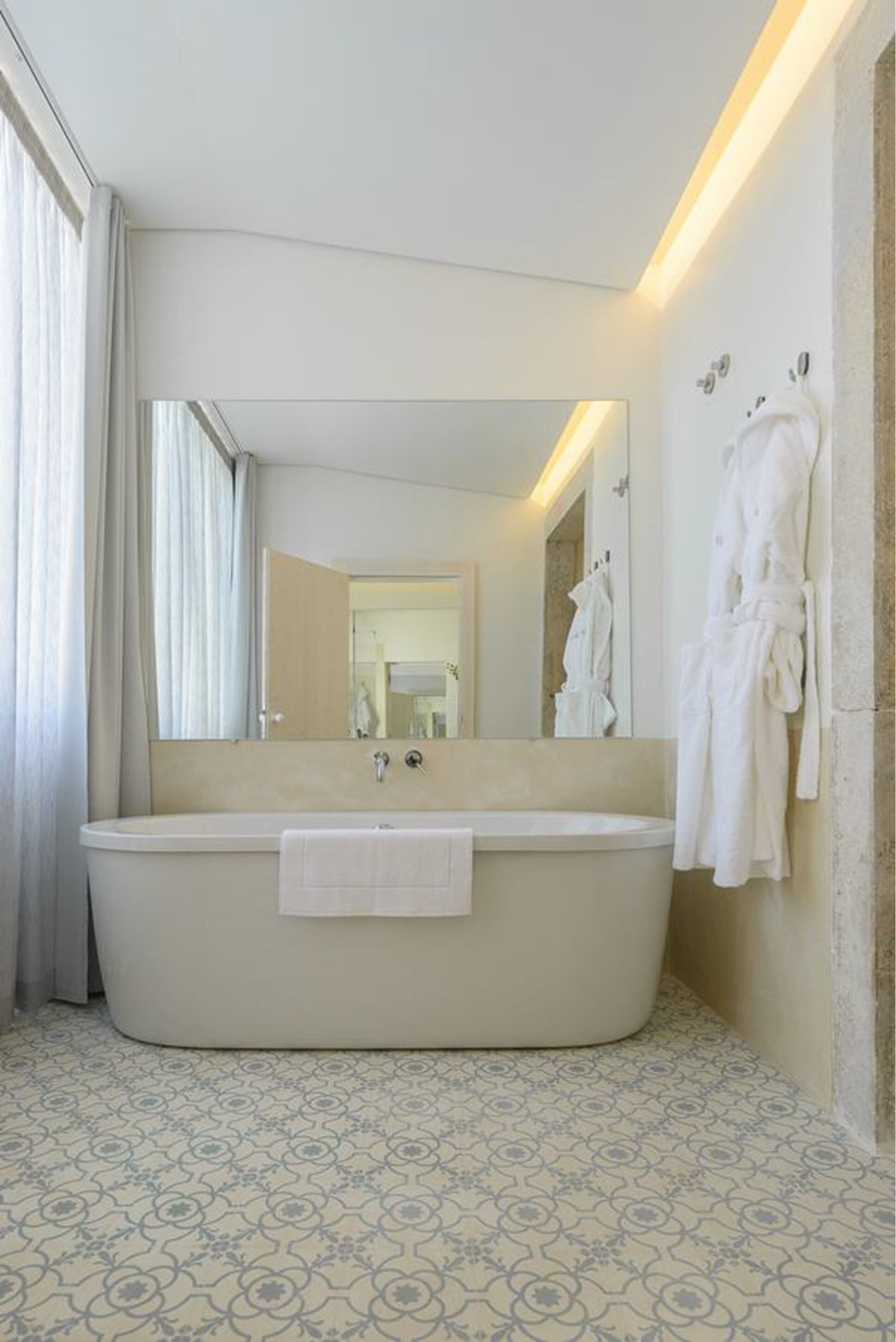 Un baño moderno con una bañera independiente, un espejo grande y un perchero con batas.