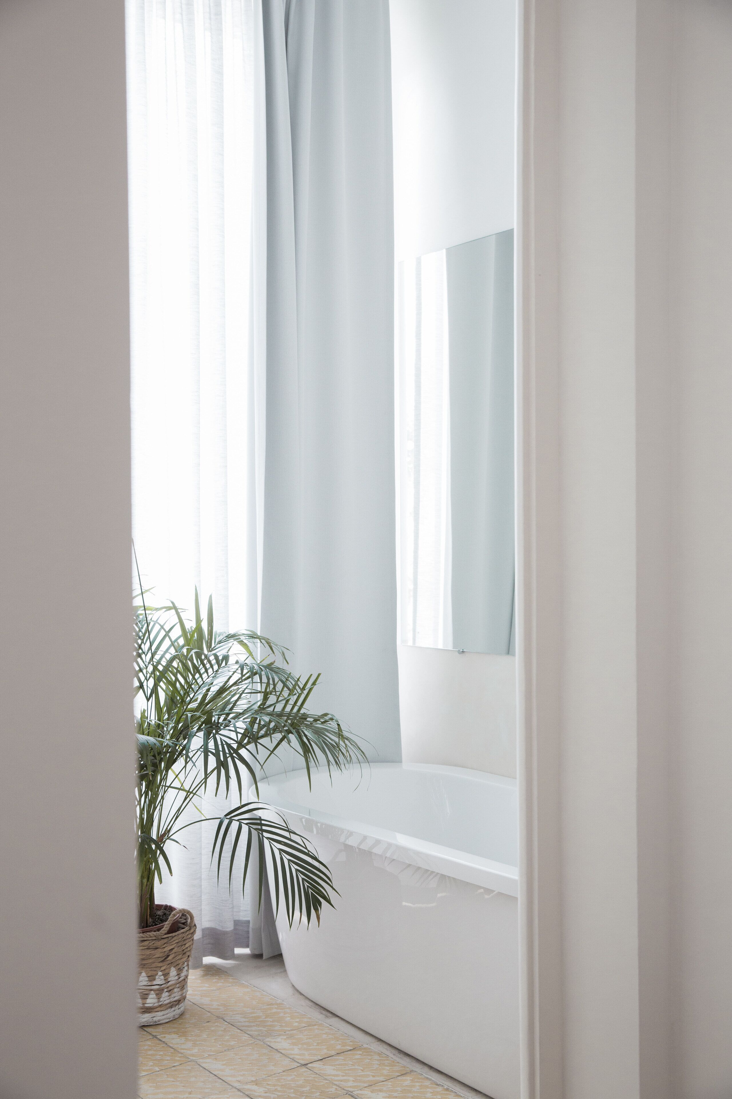 Ein Badezimmer mit Badewanne, einer Topfpflanze und einem Fenster mit Vorhängen.
