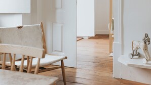 A room with a wooden floor, a white chair, a table, and a small shelf with a horse figurine.