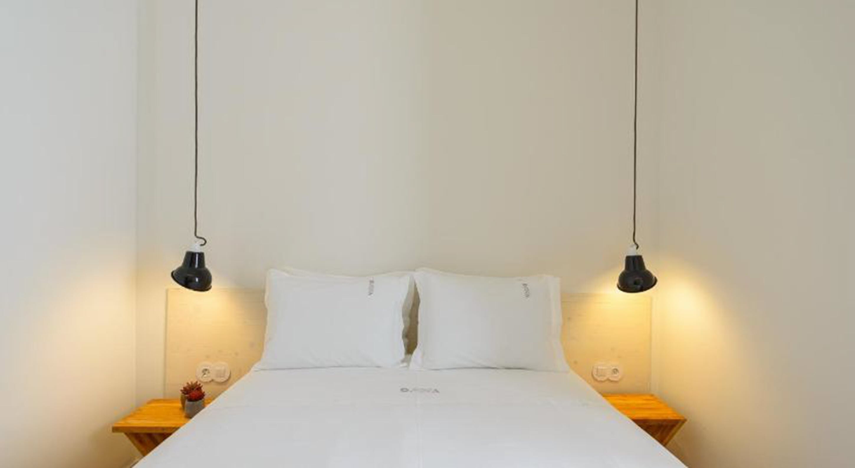 Een bed met witte lakens, twee nachtkastjes en twee hanglampen.