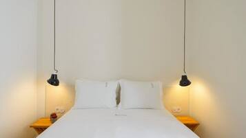 Een bed met witte lakens, twee nachtkastjes en twee hanglampen.
