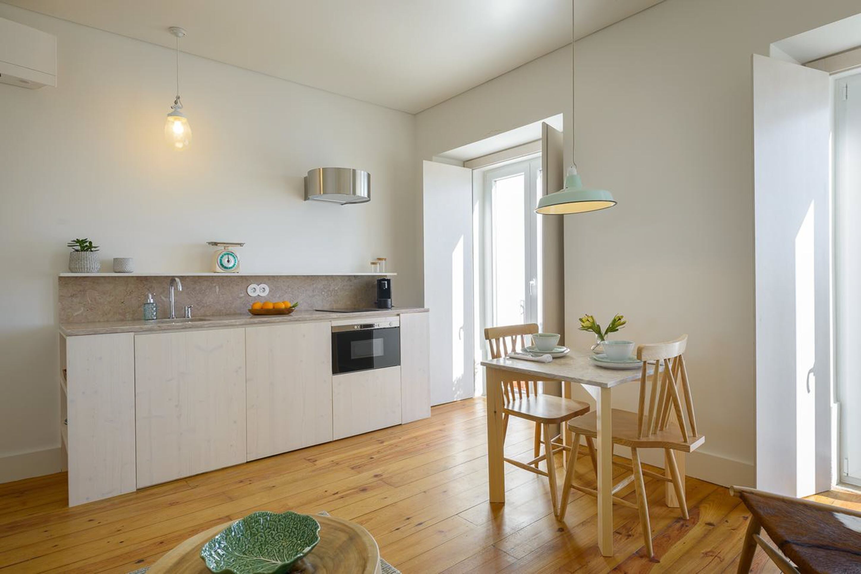A modern kitchen with white cabinetry, a wooden dining table, and a pendant light.