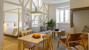 A modern, well-lit room with a bed, a sofa, a dining table with chairs, and a hanging light fixture.
