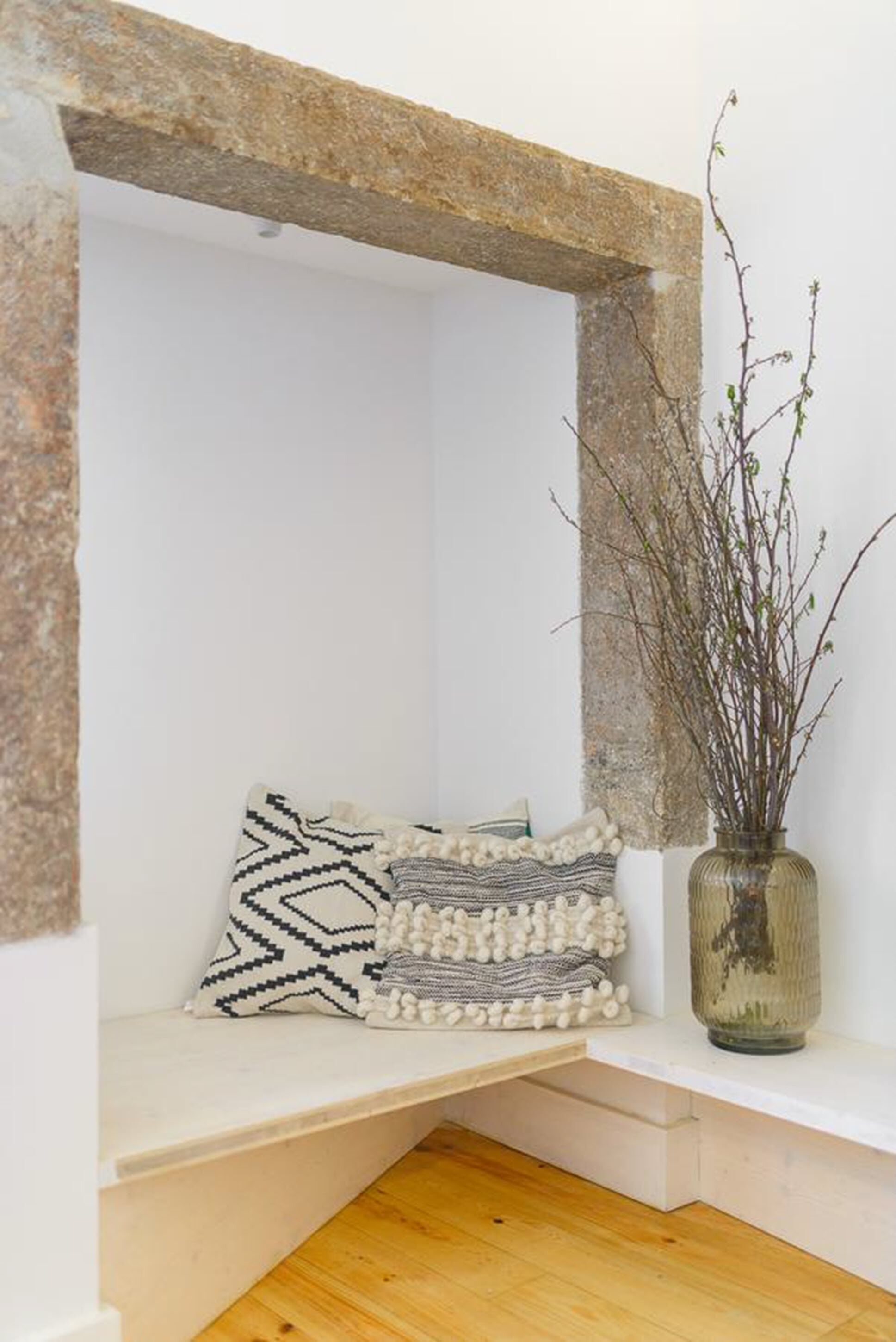 Un coin de pièce avec une arche en pierre, un banc agrémenté de coussins à motifs et un vase décoré de branches.