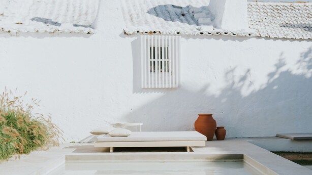 A pool area with a white building, a window, and a small table with a pot.