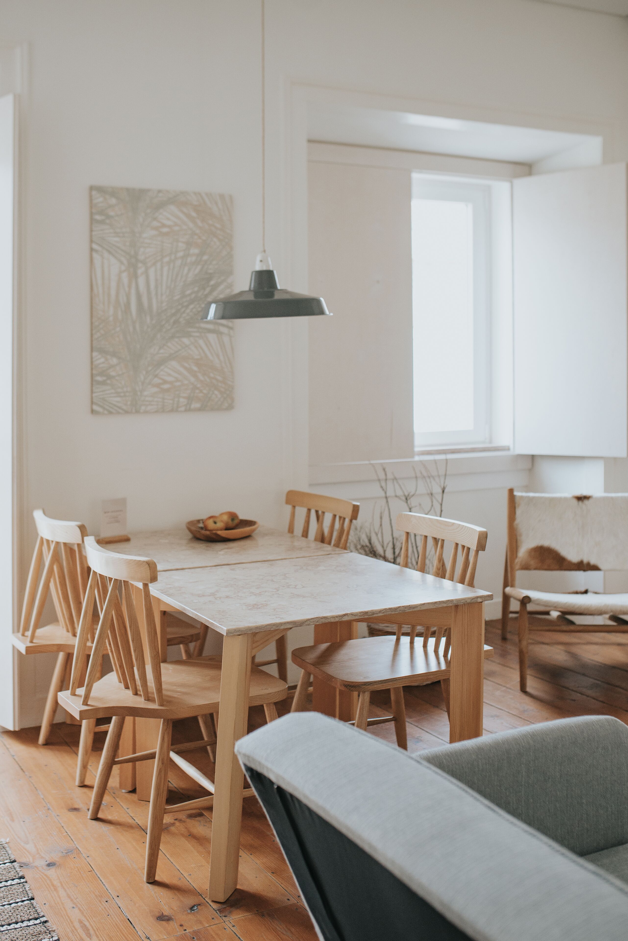 A dining area with a wooden table and chairs, a hanging pendant light, and a window with natural light.