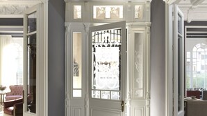 Un amplio pasillo con una puerta blanca que da a un comedor, con una araña y vistas al exterior.