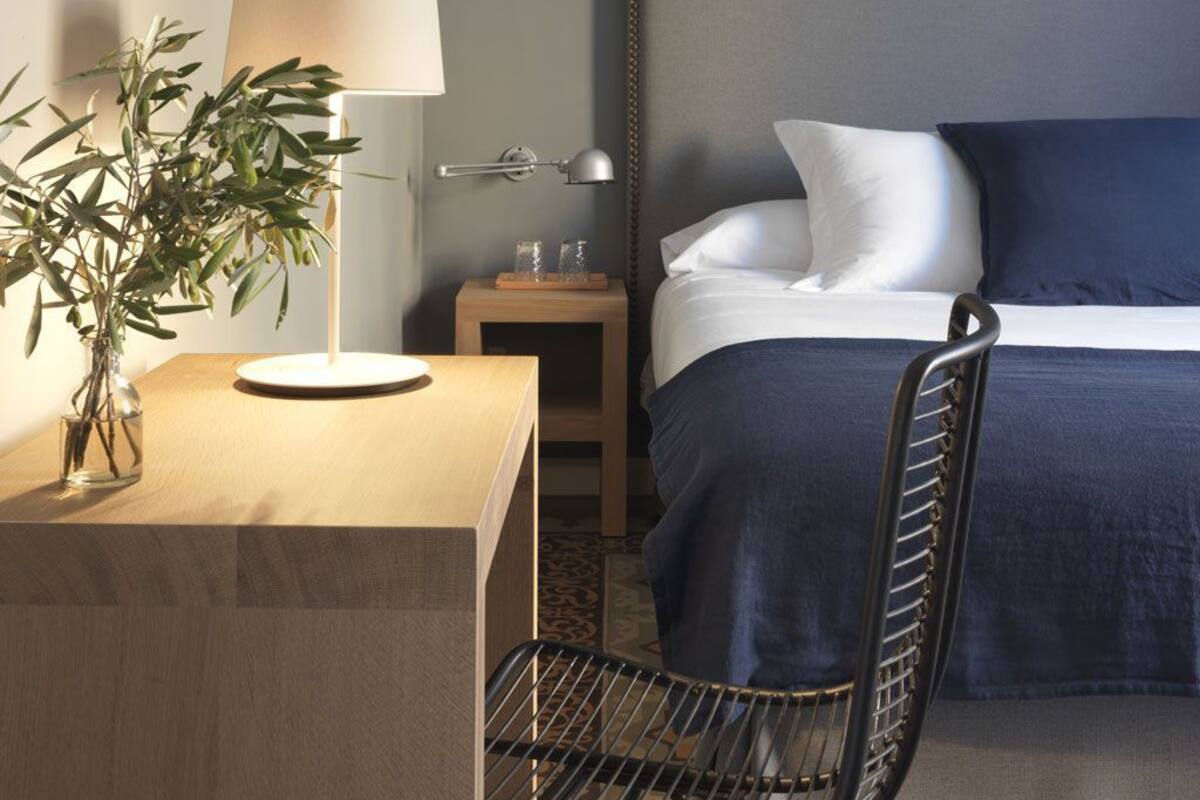 Une chambre d’hôtel bien rangée, avec un lit, une table de chevet, une lampe et une chaise.