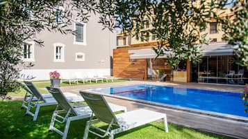 A swimming pool with lounge chairs, a wooden deck, and a building with a modern facade.