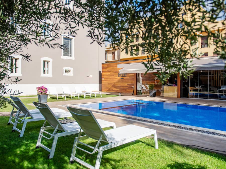 A swimming pool with lounge chairs, a wooden deck, and a building with a modern facade.