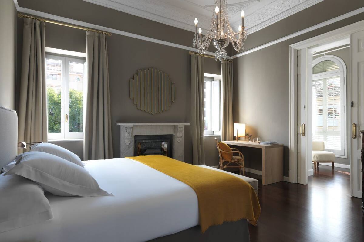 Une chambre à coucher avec un grand lit, un bureau, une chaise, une cheminée et un lustre.