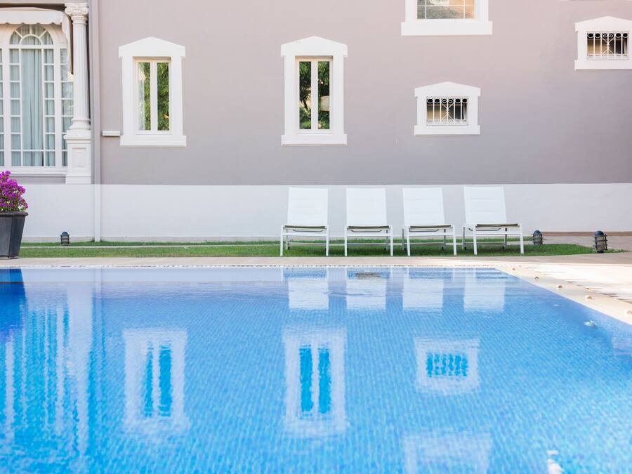 A swimming pool with a clear blue water surface, surrounded by white chairs and a building with white trim and windows.