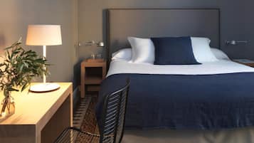 A hotel room with a bed, bedside table, lamp, chair, and a decorative plant.