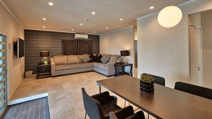 A modern living room with a sofa, a dining table, and a TV mounted on the wall. - Sesoko  Villa (Motobu)