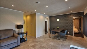 A modern living room with a sofa, a dining table with chairs, recessed ceiling lights, and a patterned wall. - Sesoko  Villa (Motobu)