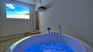 A modern bathroom with a large bathtub, a shower, and a projection screen displaying a beach scene. - Sesoko  Villa (Motobu)