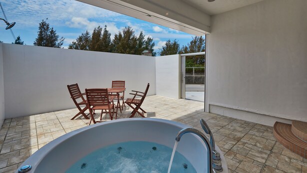 A modern outdoor patio with a hot tub, wooden chairs, and a table. - Sesoko  Villa (Motobu)