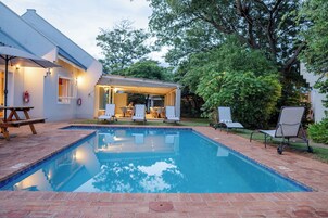 Una piscina con zona de patio, mobiliario exterior y una sección cubierta con mesa y sillas.