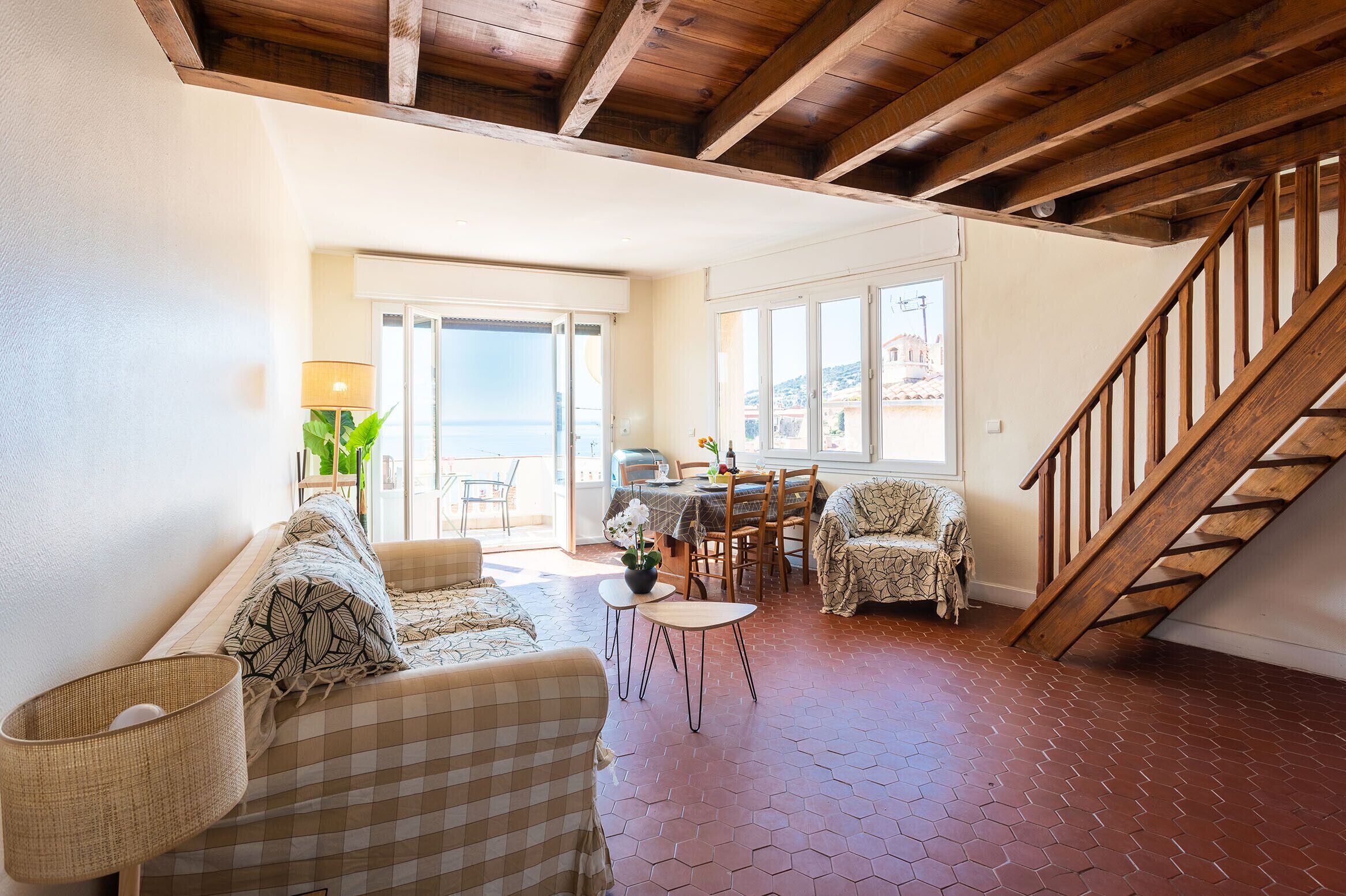 A spacious living area with a wooden staircase, a dining table with chairs, and a view of the outdoors.