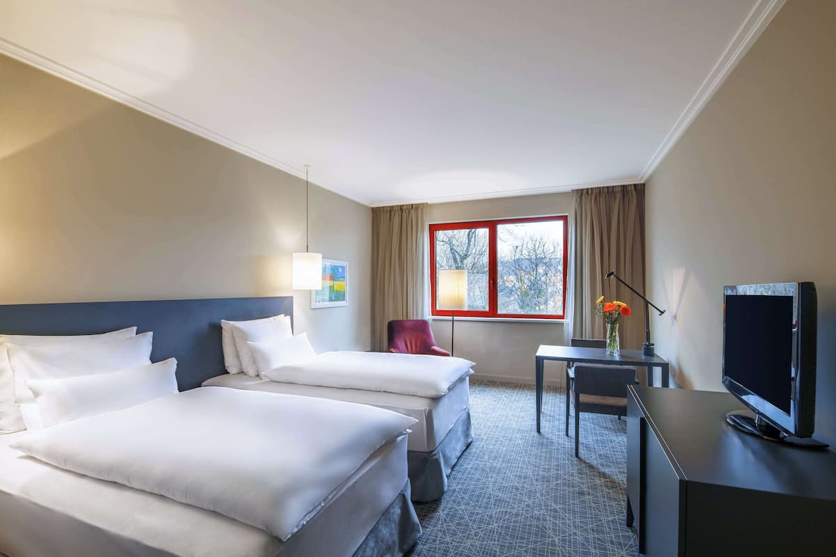 A hotel room with two beds, a desk, a TV, and a window with curtains.