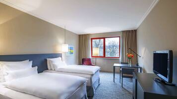 A hotel room with two beds, a desk, a TV, and a window with curtains.