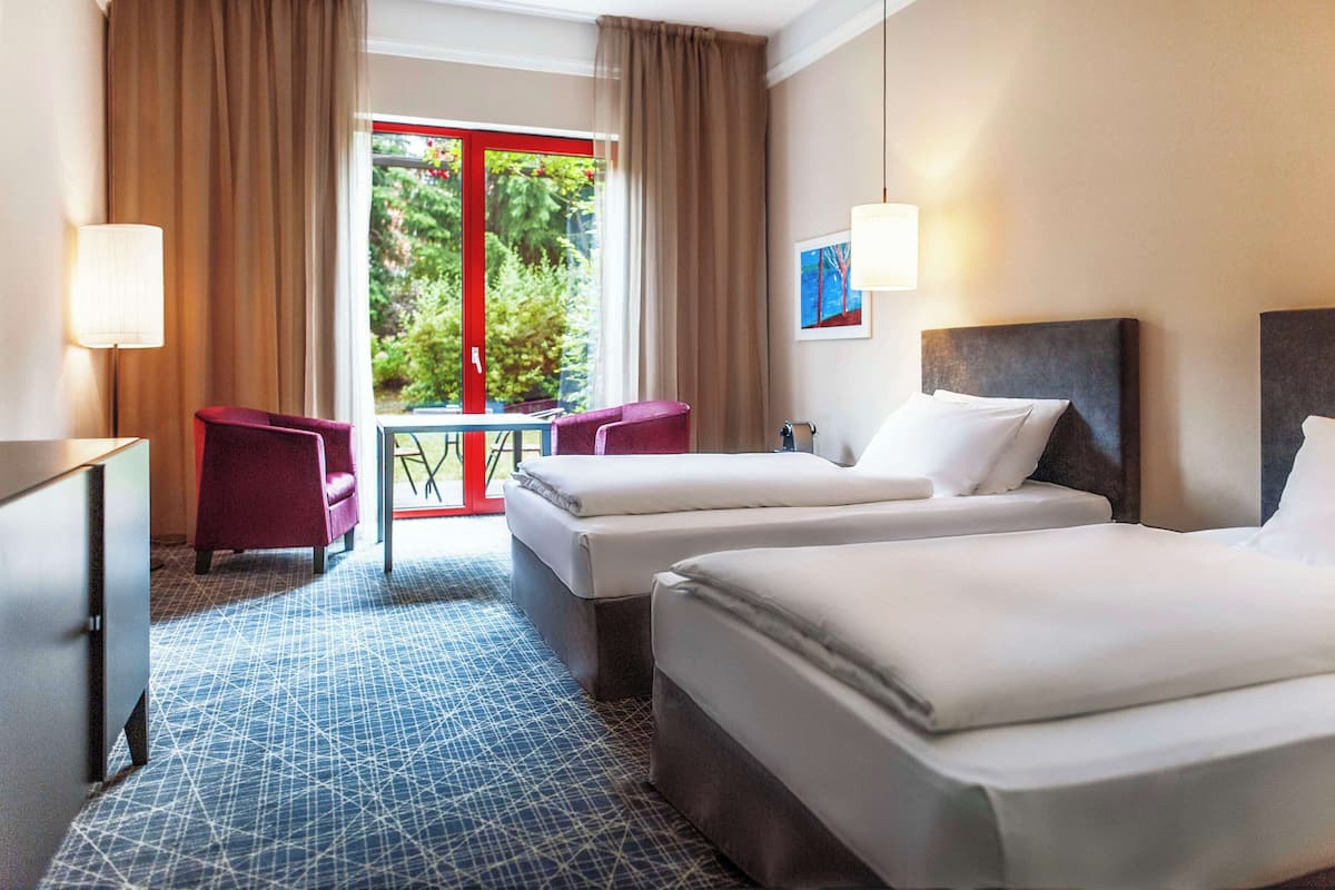 A hotel room with two beds, a desk, a chair, and a window with curtains.