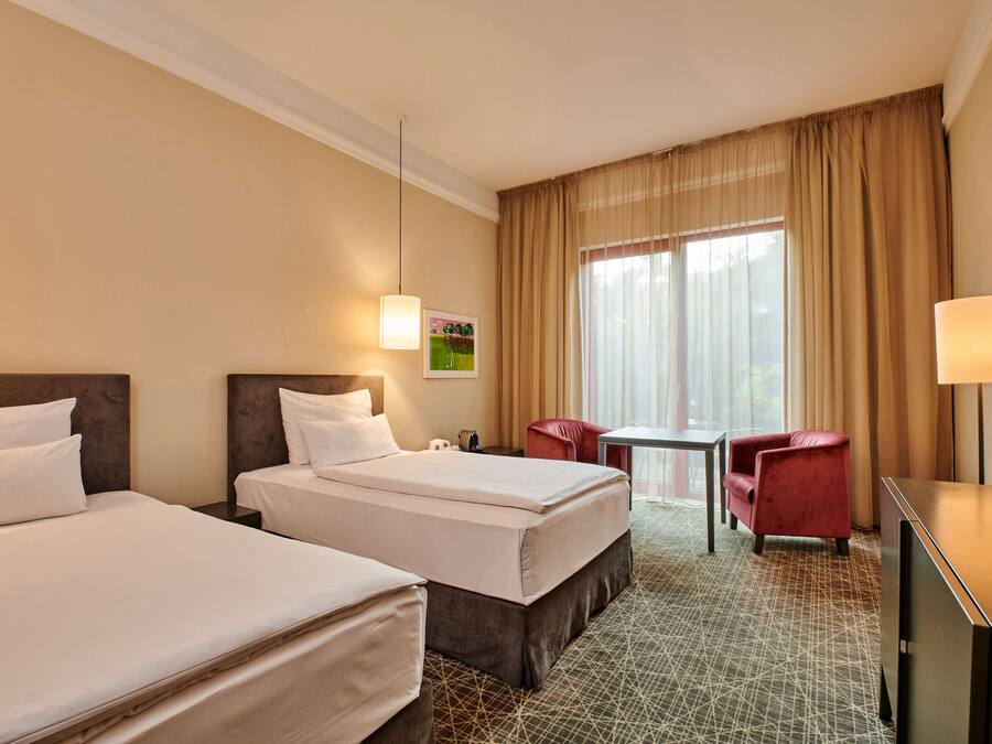 A hotel room with two beds, a desk, a chair, and a television.