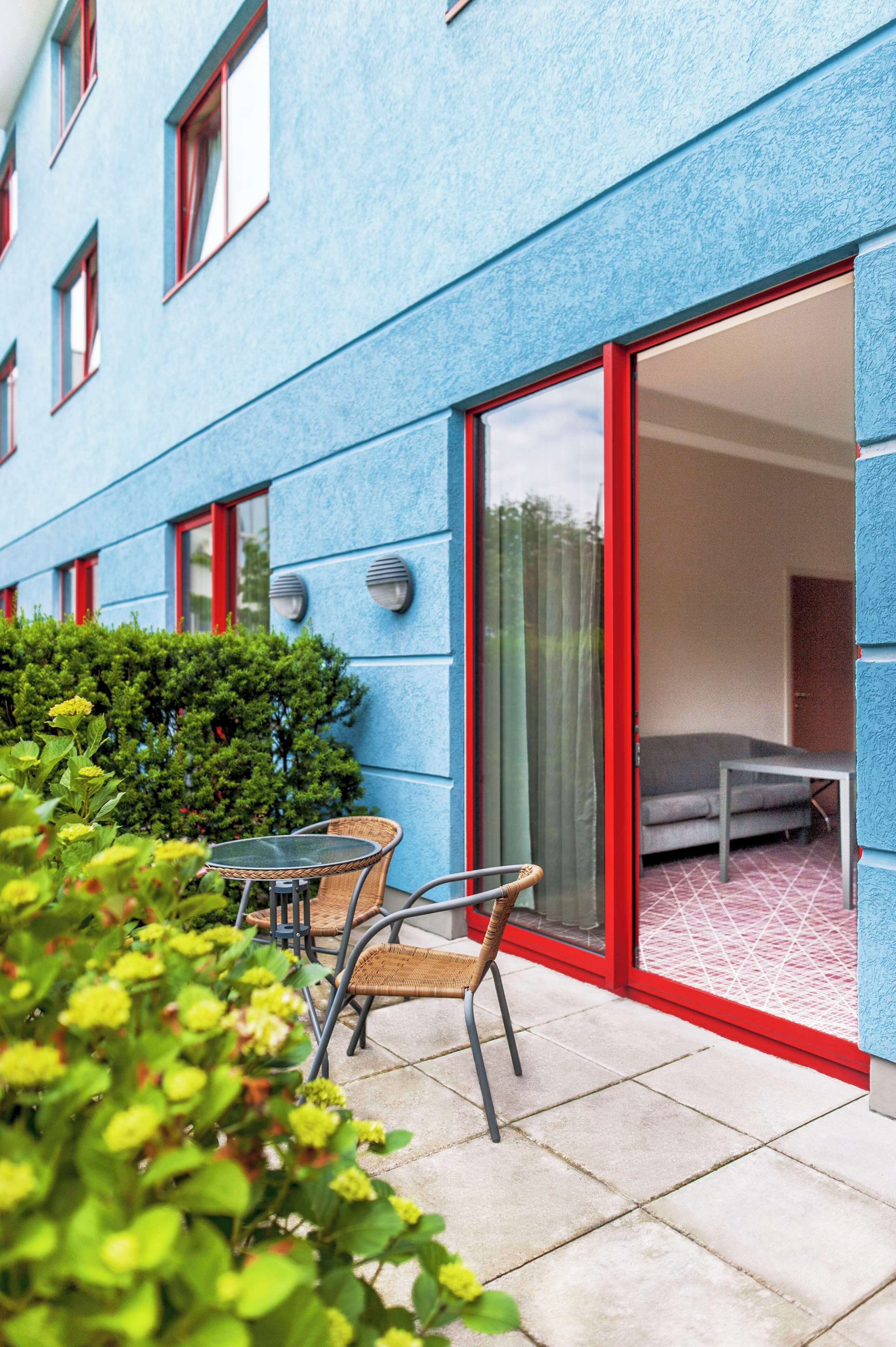 A blue building with a sliding glass door leading to a room with a gray sofa and a small table.
