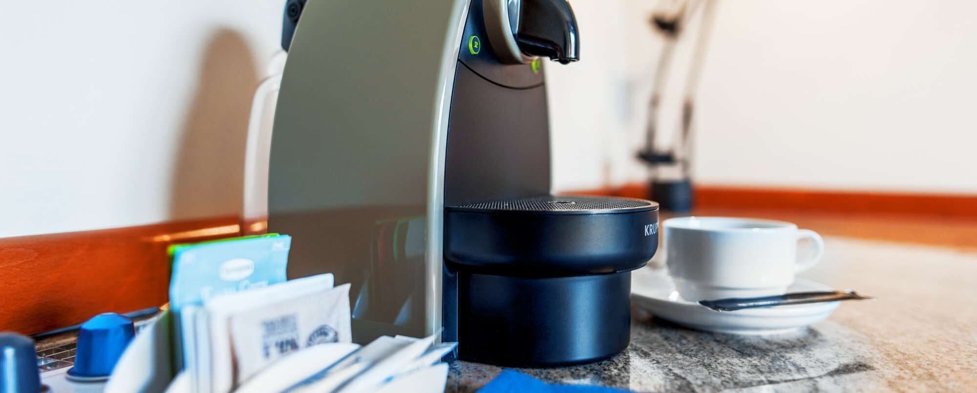 Una cafetera, una taza y algunas cápsulas de café sobre una mesa.