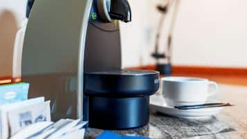 Una cafetera, una taza y algunas cápsulas de café sobre una mesa.