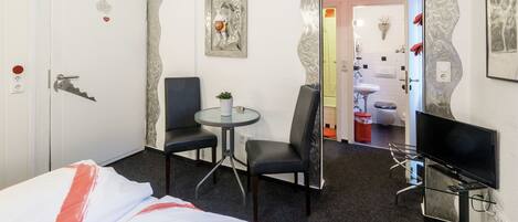 Hotellihuoneessa on sänky, työpöytä, tuoli, televisio ja kylpyhuone, joka näkyy holvikaaren läpi.