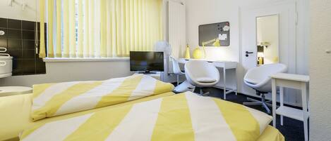 A hotel room with a bed, a desk, a chair, a TV, and a bathroom.