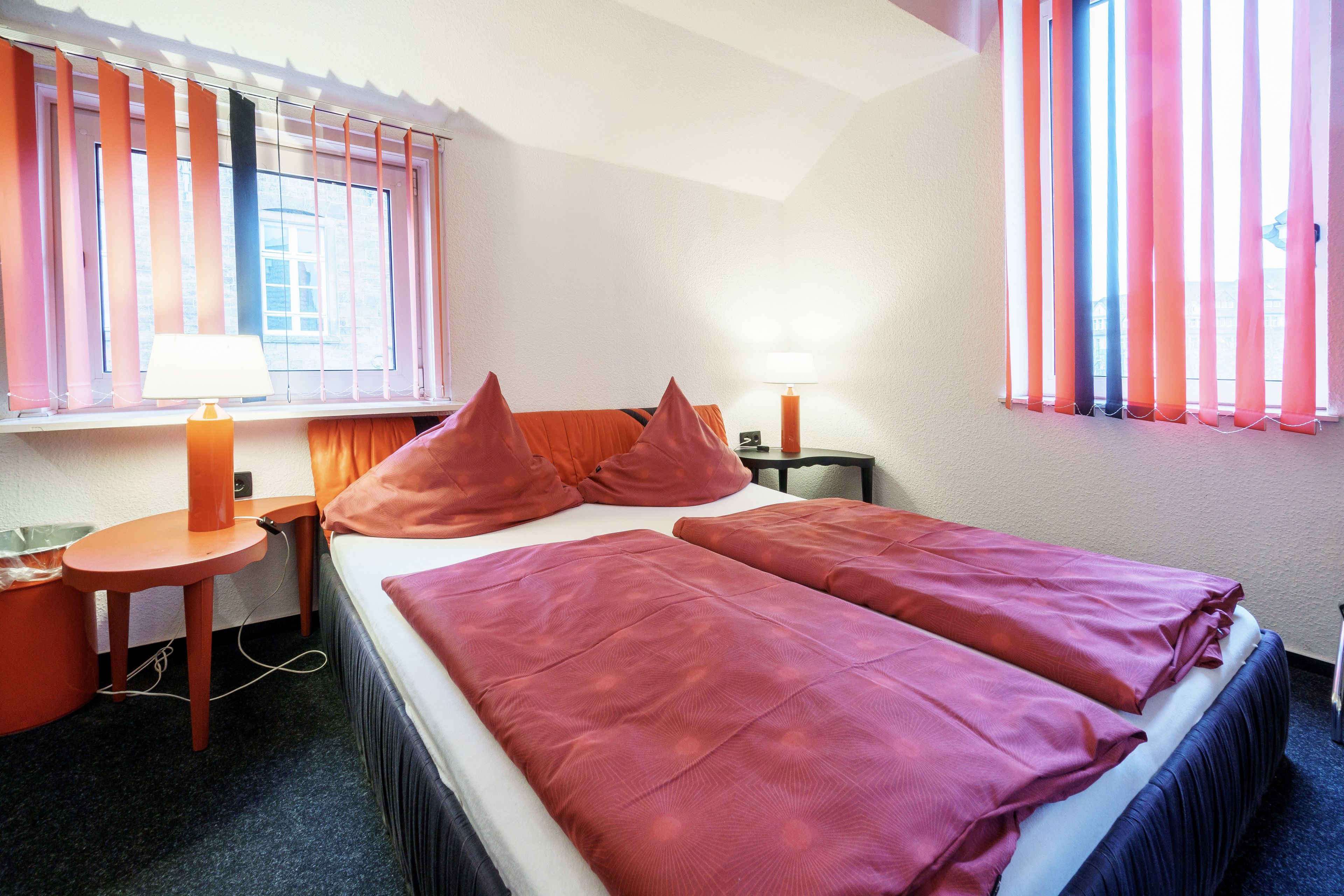 Una habitación de hotel con una cama, dos mesitas de noche, una lámpara y una ventana con cortinas.