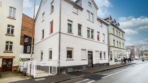 Edifici blanc amb diverses finestres i una porta, situat a una cantonada de carrer amb vorada i algunes bicicletes aparcades a prop.