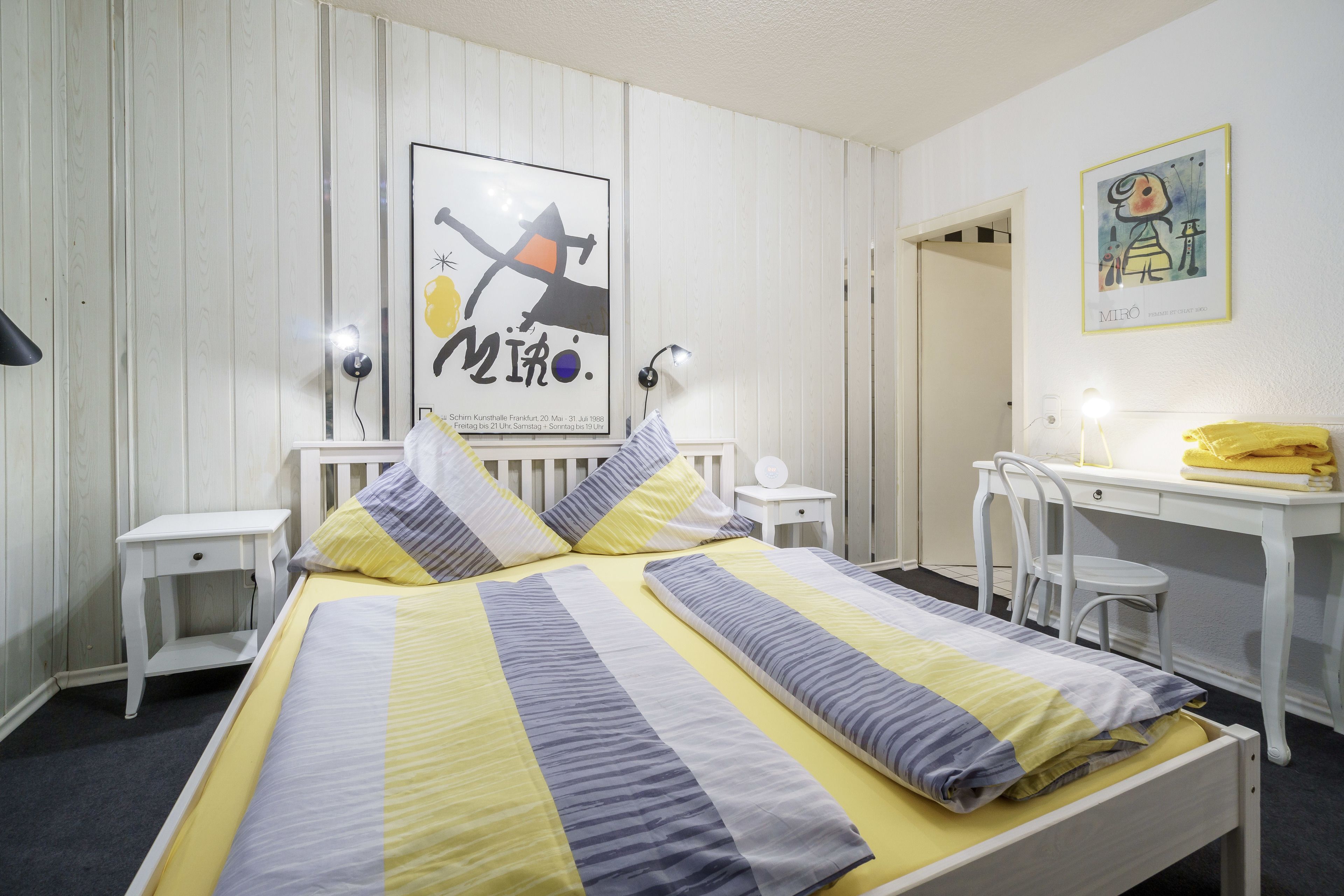 A neatly arranged bedroom with a bed, bedside tables, a desk, and chairs.