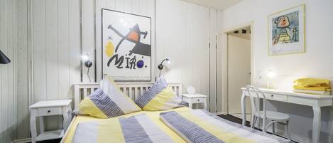 A neatly arranged bedroom with a bed, bedside tables, a desk, and chairs.