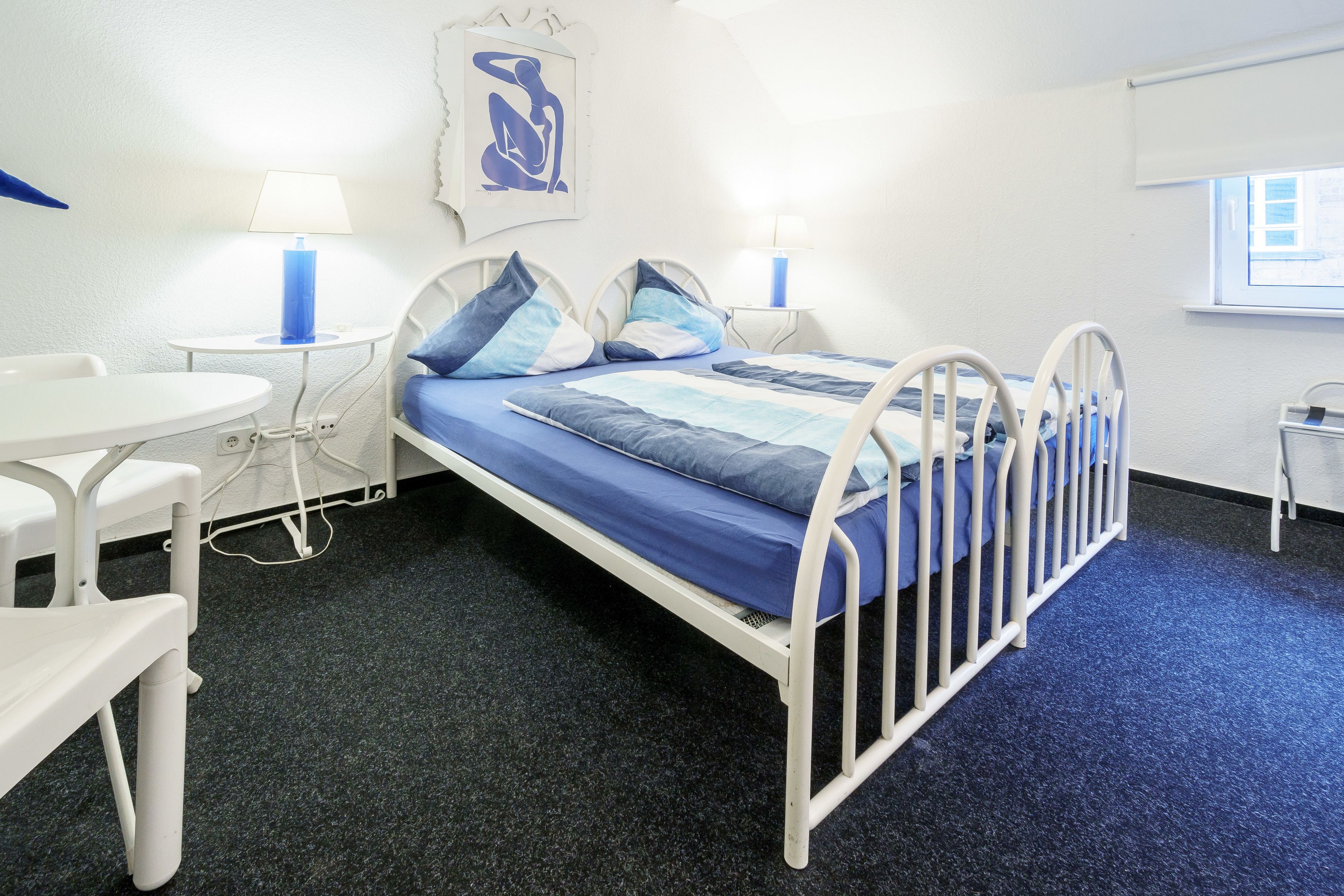 Une chambre avec un lit simple, décorée dans des tons de bleu et de blanc, comprenant un bureau et deux lampes de chevet.