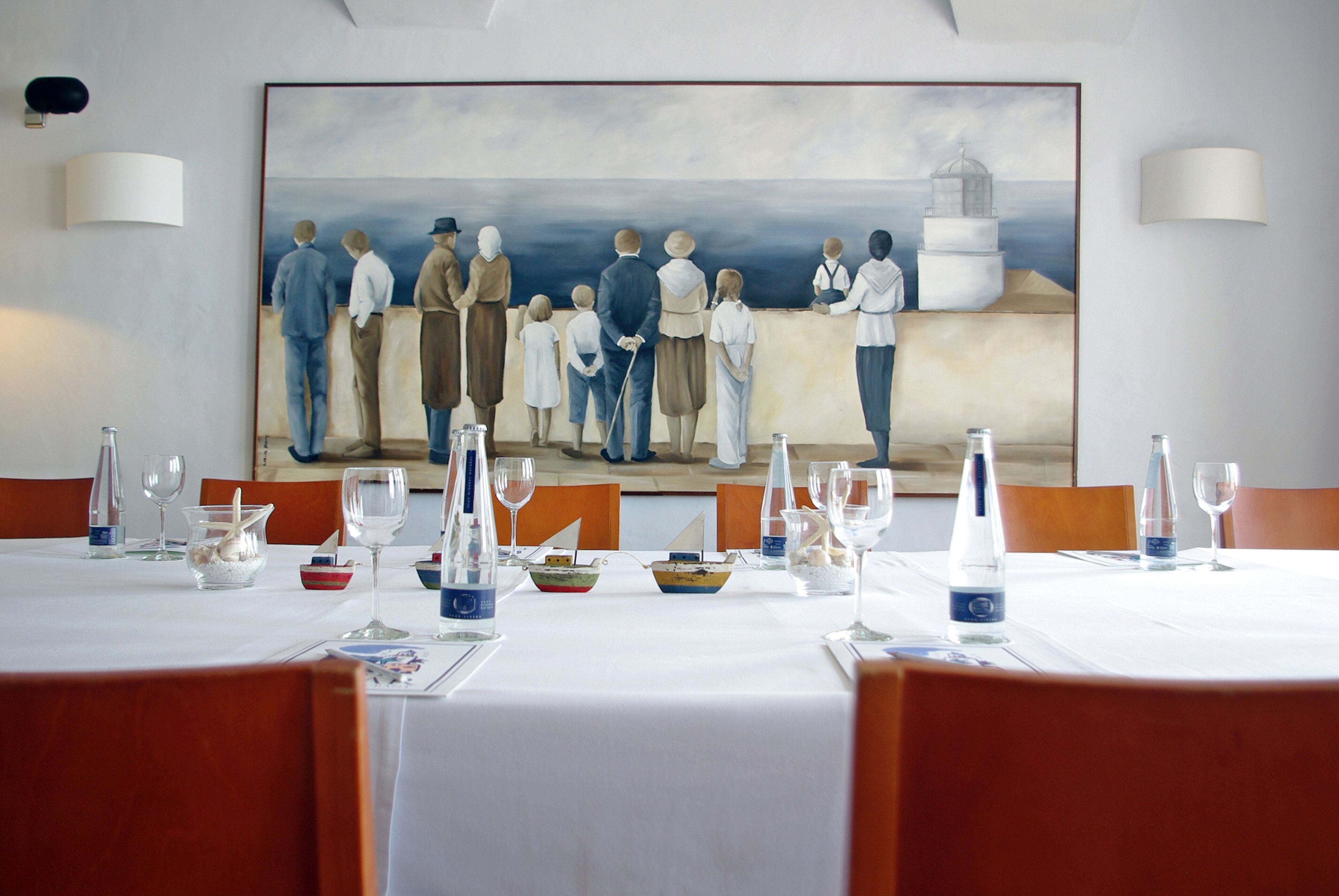 A dining area with a table set for six, a large painting on the wall, and a view of the sea.