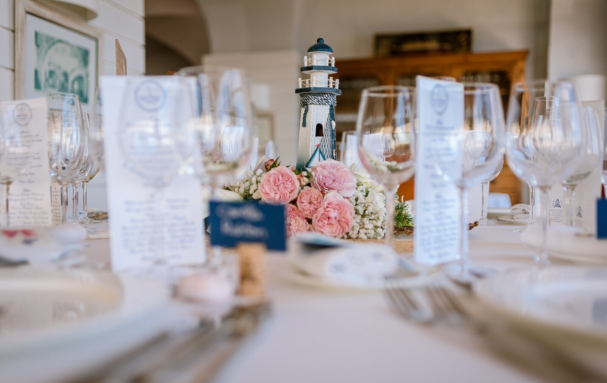 A table set for a formal event with a decorative lighthouse centerpiece, menus, and wine glasses.