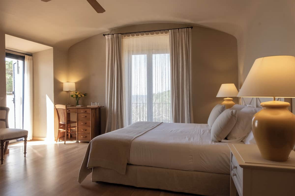 Ein Schlafzimmer mit einem großen Bett, zwei Nachttischlampen, einem Schreibtisch mit Stuhl und einem Fenster mit Vorhängen.
