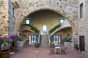 Un patio de piedra con arco, una escalera central, plantas en macetas y asientos al aire libre.