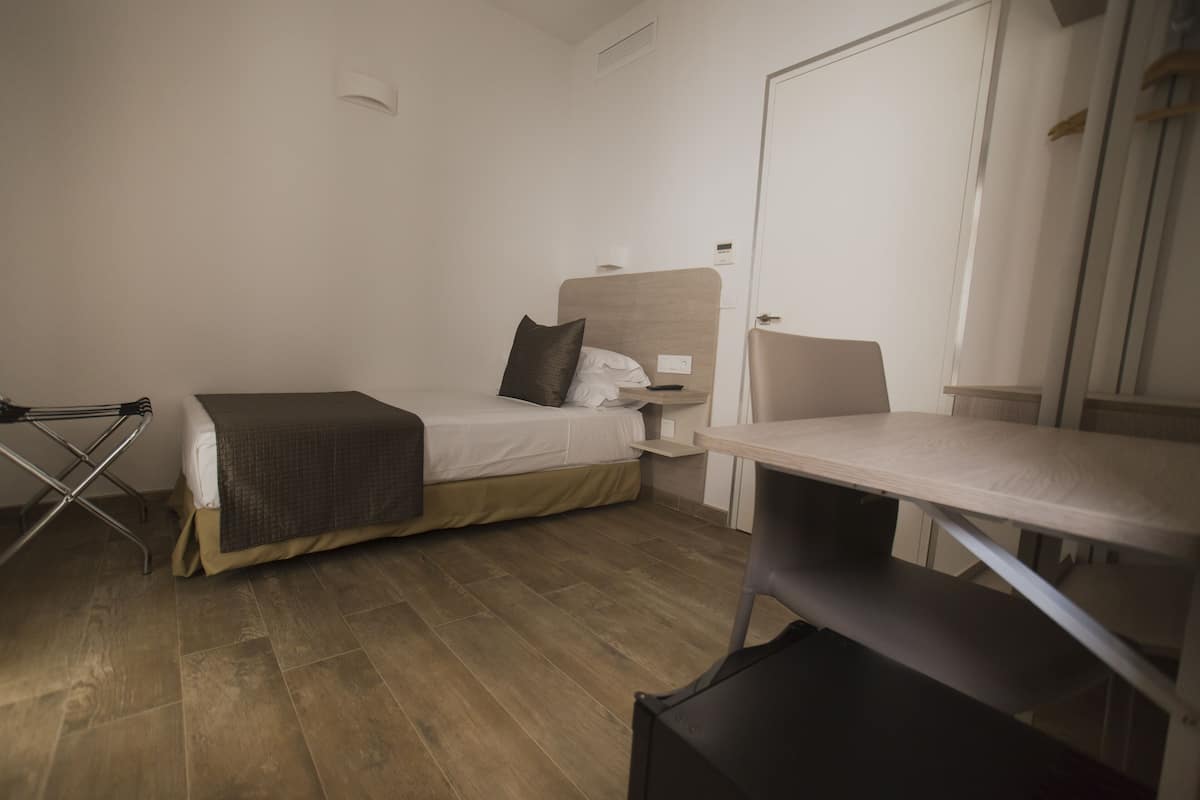 A compact hotel room with a single bed, a desk, a chair, and a wardrobe.