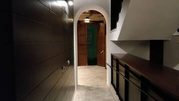 Un couloir se termine par une porte en bois, une enseigne est placée au-dessus, et un escalier se trouve sur la droite.